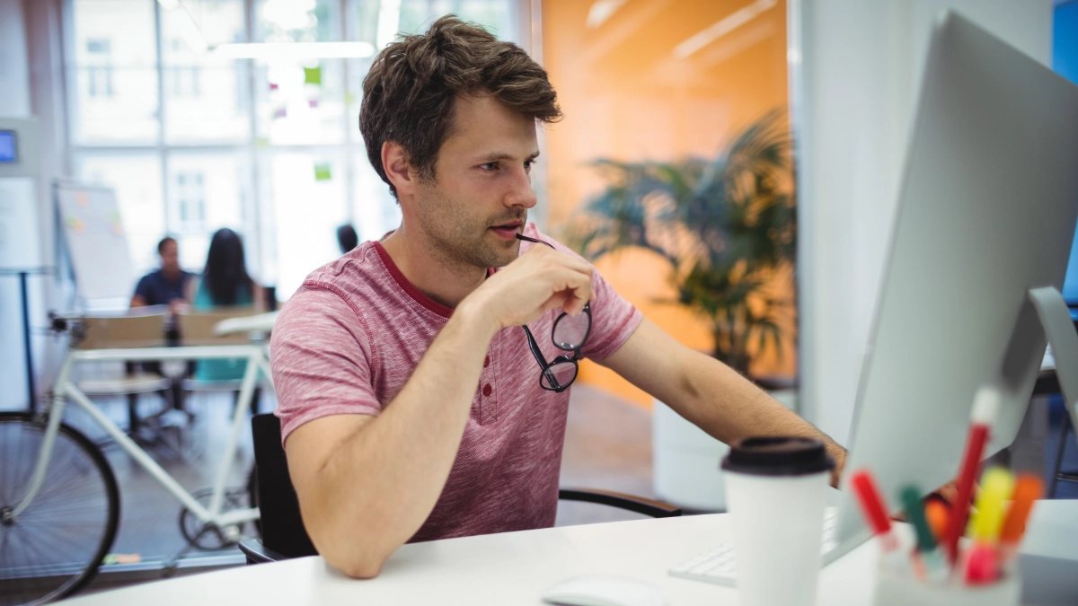 Man in office setting looking at desktop computer screen pondering
